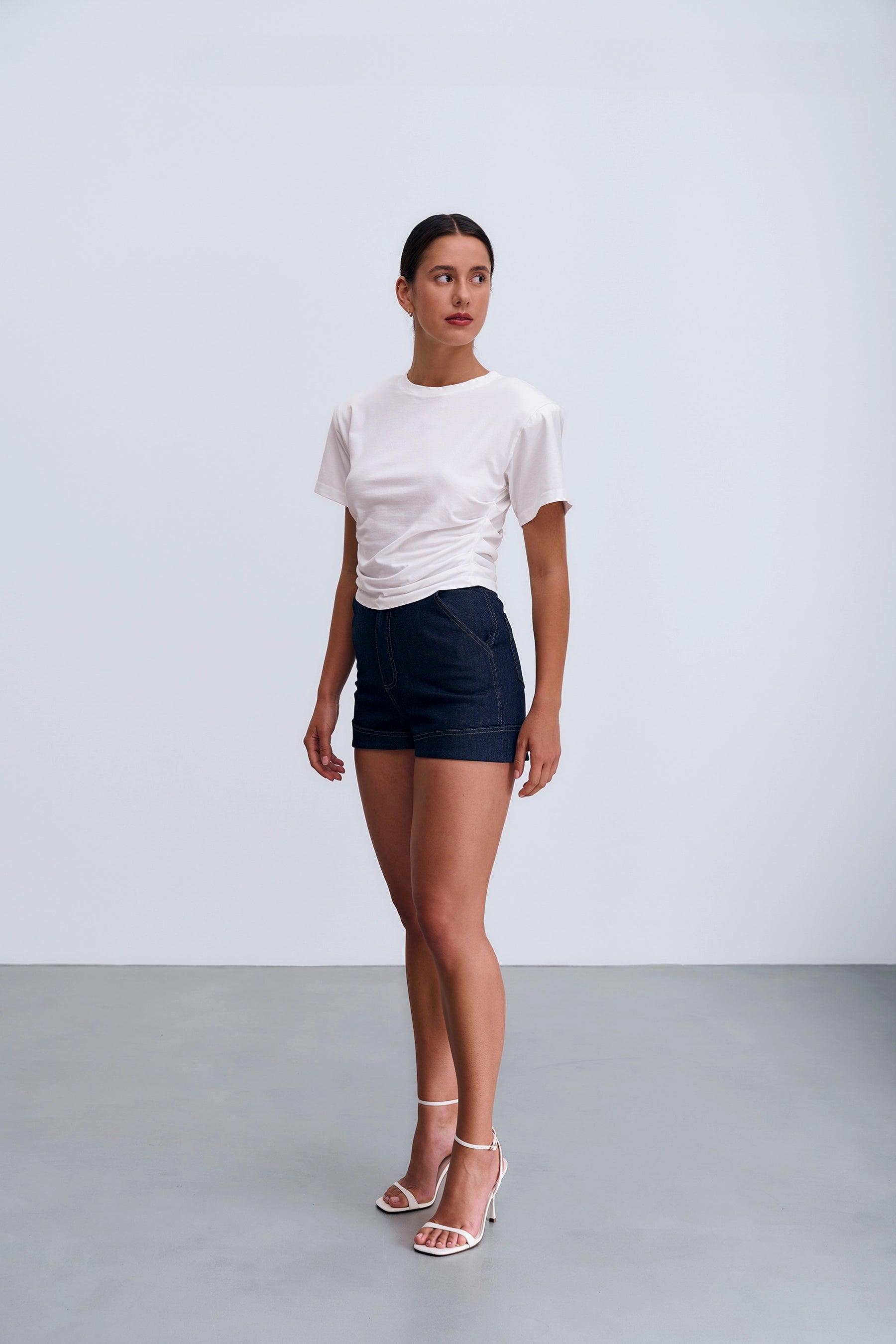 Siena T‑shirt White widoczny z boku – biały T‑shirt z dopasowanymi bocznymi marszczeniami i poduszkami na ramionach nadającymi sylwetce strukturę.