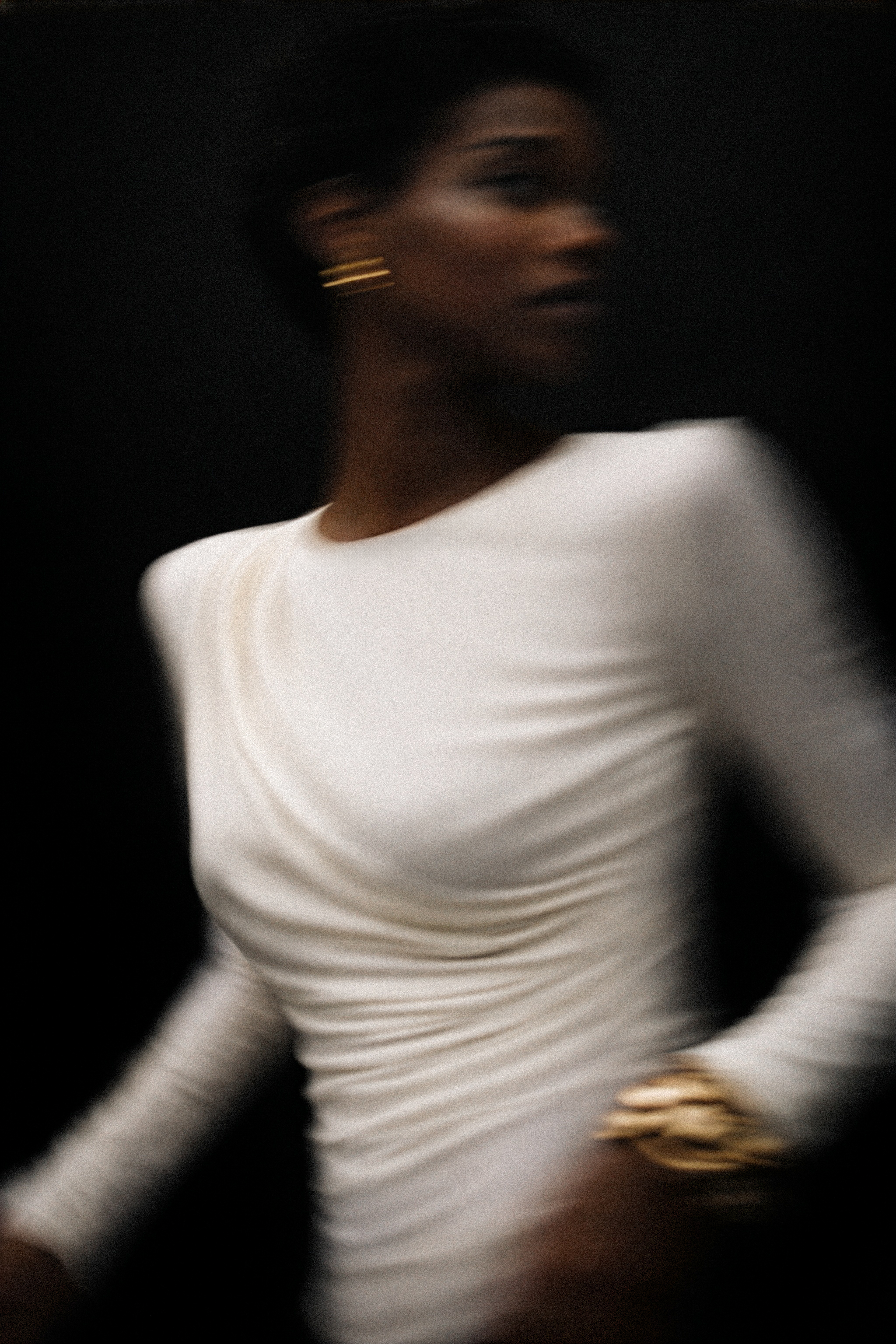 Modelka w jasnym, dopasowanym body z długim rękawem, w dynamicznym, lekko rozmytym ujęciu na ciemnym tle.