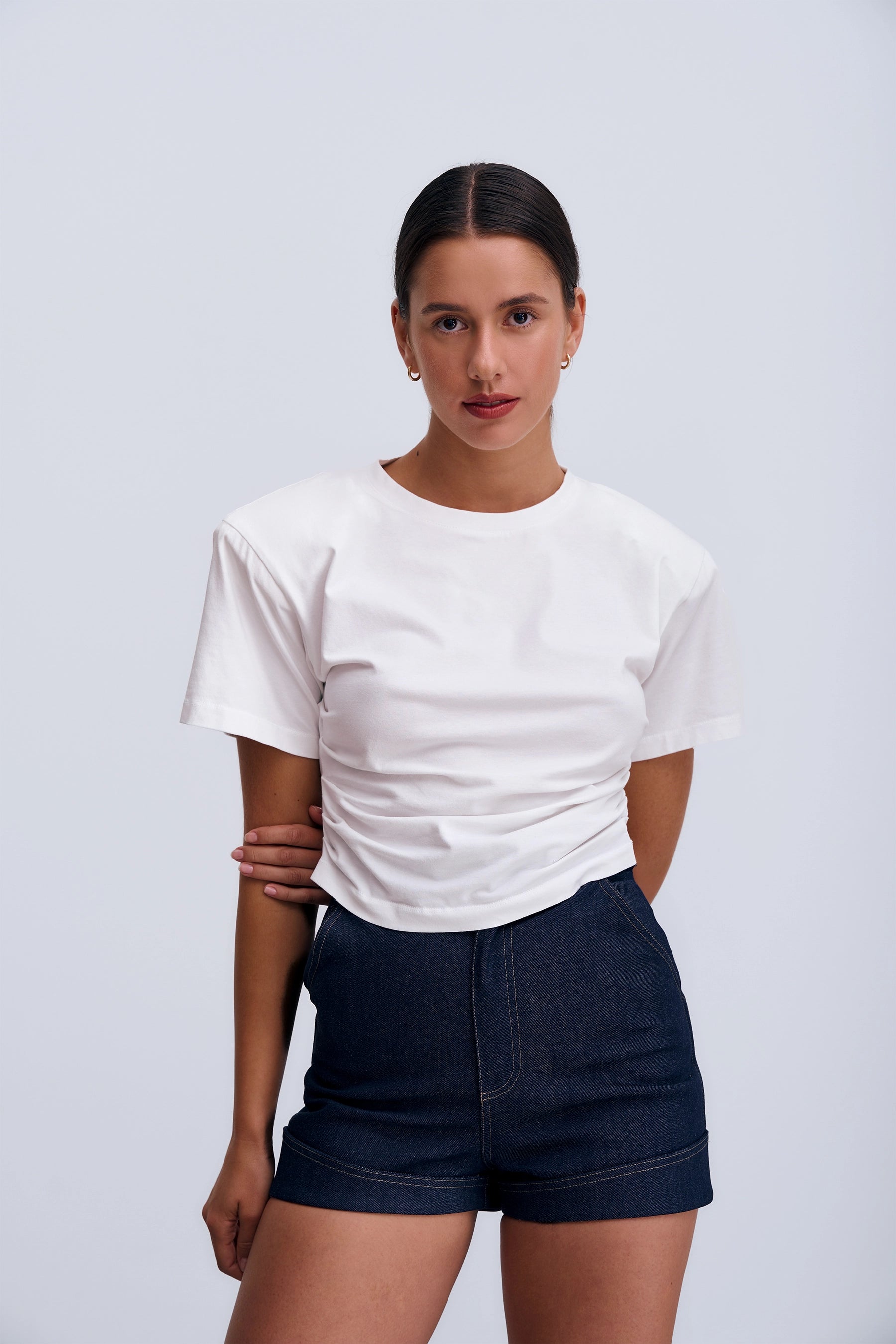 Siena T‑shirt White – biały damski T‑shirt z okrągłym dekoltem, bocznymi marszczeniami modelującymi sylwetkę i poduszkami na ramionach.