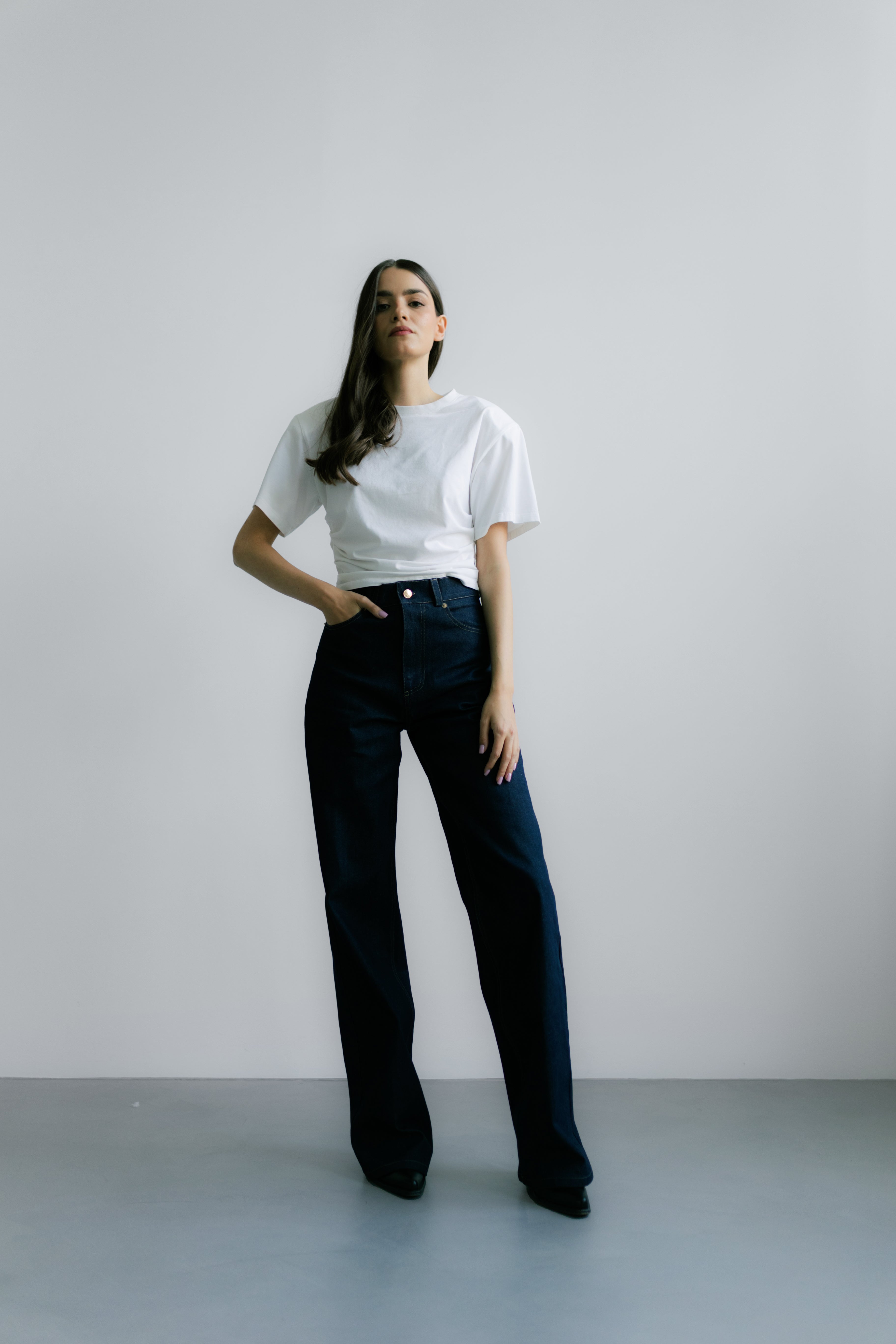 Modelka w Siena T‑shirt White – biały T‑shirt z poduszkami na ramionach, krótki fason i nowoczesny minimalistyczny wygląd.